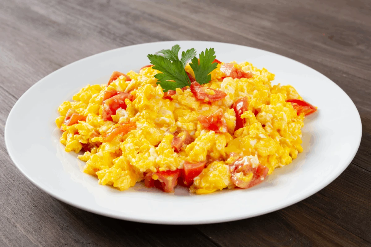 Jajecznica z serkiem wiejskim i pomidorami na białym talerzu